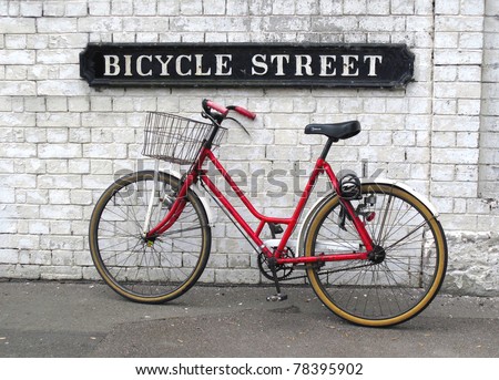 Bicycle Street sign with a red bicycle leaning against a white painted brick wall