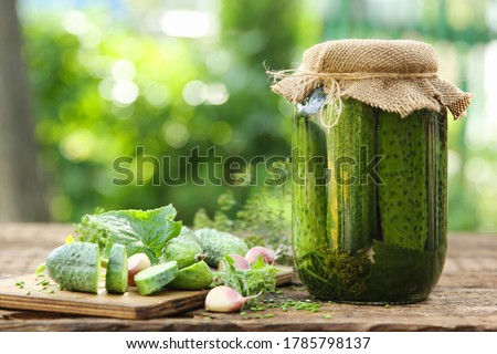 Preservations, conservation. Salted, pickled cucumbers in a jar on an old wooden table in the garden. Summer, sunny day. Cucumbers, herbs, dill, garlic. Rustic. Background image, copy space,horizontal