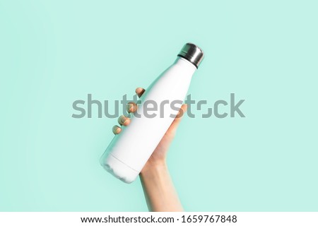 Close-up of female hand, holding white reusable steel stainless eco thermo water bottle with mockup, isolated on background of cyan, aqua menthe color. Be plastic free. Zero waste.