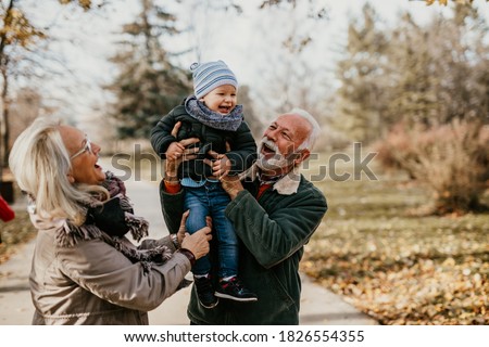 Happy good looking senior couple husband and wife walking and playing with their adorable grandson in public city park
