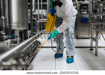 Exterminator in industrial plant spraying pesticide with sprayer. Disinfection of the factory due to the coronavirus epidemic. Foto d'archivio © 