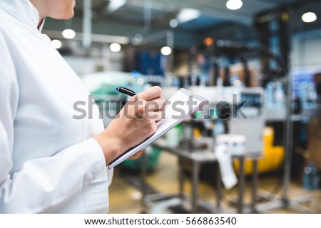 Young happy female worker in factory writing notes about water bottles or gallons before shipment. Inspection quality control. Selective focus on hand. Foto stock © 