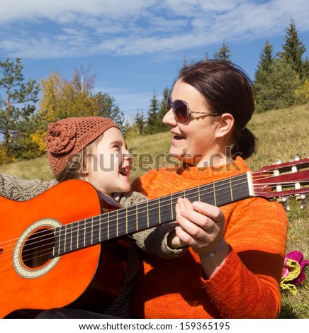 Happy family, young beautiful mother and her little daughter with guitar outdoor