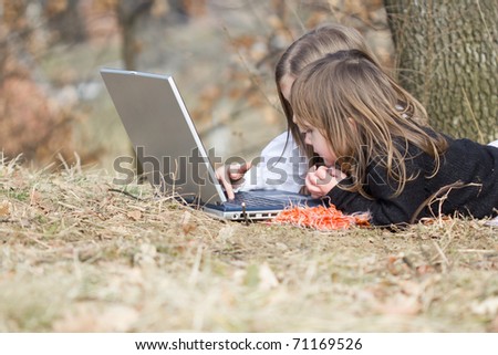 Two little girls playing on computer outside in autumn