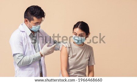 Asian people, Man doctor wearing medical mask and gloves giving coronavirus (COVID-19) vaccine to female on brown background. Asian woman getting vaccinated by medical professional.