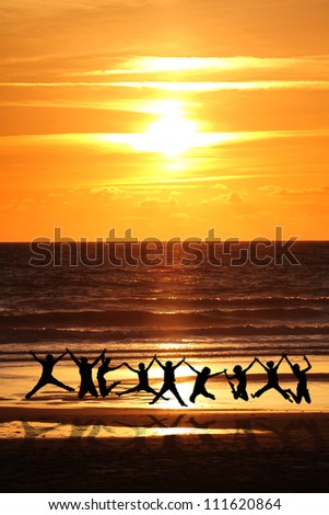 silhouette of friends jumping on beach in sunset light