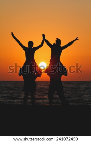 silhouette teens sitting on shoulders of friends in sunset
