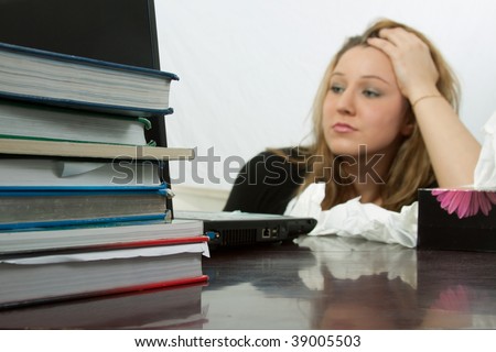 Blond young caucasian woman sitting at desk in front of laptop computer  with a box of tissues with focus on a pile of text books