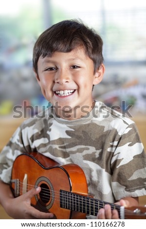 A happy smiling young boy plays his guitar or ukulele