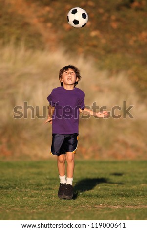 Boy playing with soccer ball in early evening sunlight with Fall or Autumn foliage behind him.