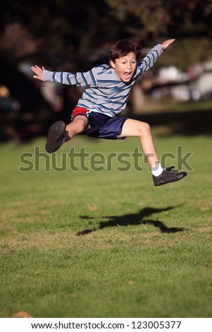Happy boy jumping in the park - authentic action - copy space bottom