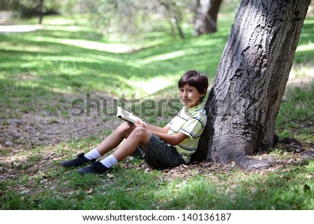 Young boy sitting under tree in the woods - with copy space