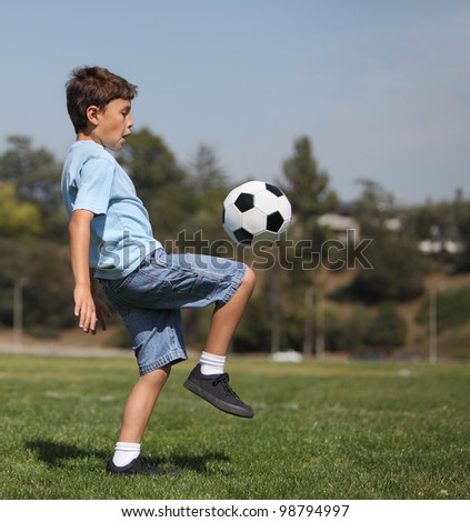 A young boy knee kicks a soccer ball in a park with copy space to right