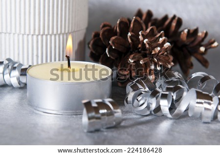 Christmas decoration with candle, silver ribbon, cones and gift box.