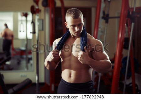 Strong man bodybuilder with towel on his neck in a gym relaxing