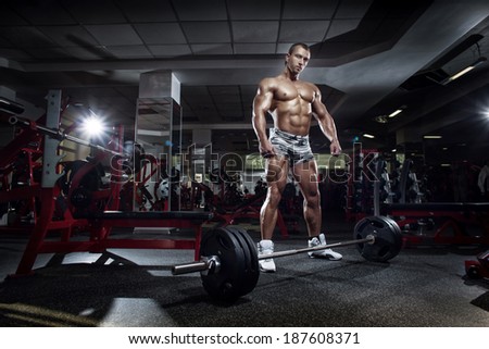 very power athletic guy standing with barbell, workout in the gym