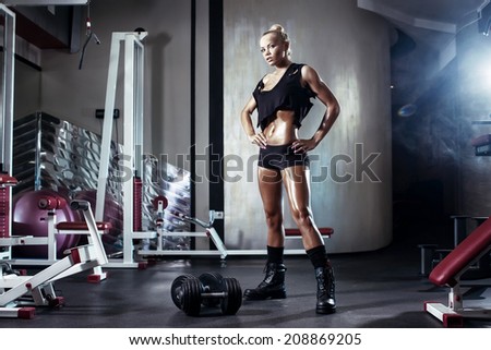fitness blonde girl posing and prepares for exercising with dumbbell in gym