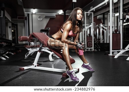 fitness girl with shaker posing on bench in the gym