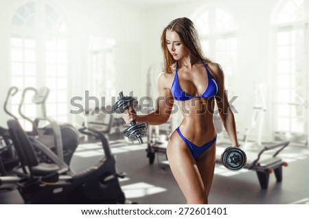 sexy busty young woman in a bikini workout training with dumbbells in gym