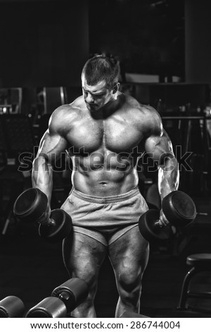 Athlete muscular bodybuilder in the gym training with dumbbells black and white