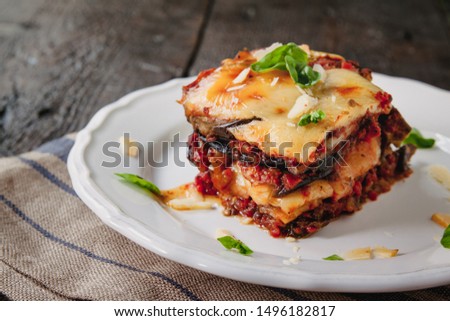 tradicional Parmigiana di melanzane: baked eggplant - italy, sicily cousine.Baked eggplant with cheese, tomatoes and spices on a white plate. A dish of eggplant is on a wooden table