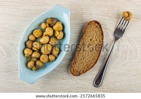 Blue oval plate with marinated champignons, slice of rye bread, mushroom strung on fork.on wooden table. Top view Imagine de stoc © 