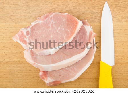 Three raw pork chops on hardboard and ceramic knife