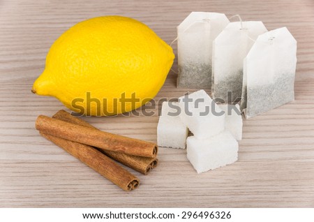 Lumps of sugar, cinnamon sticks, lemon and packets of tea on wooden table