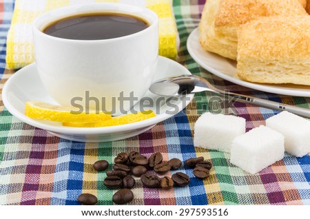 Close up of black coffee and coffee beans, lemon and sugar, flaky biscuits on tablecloth