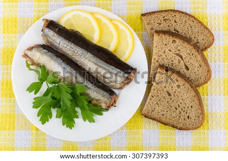 Canned fish, lemon, parsley and pieces of bread on tablecloth, top view