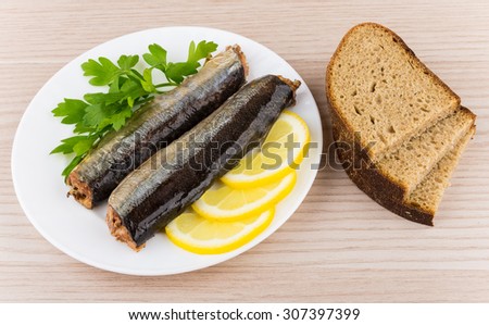 Canned fish with lemon and parsley in plate and pieces of bread on wooden table