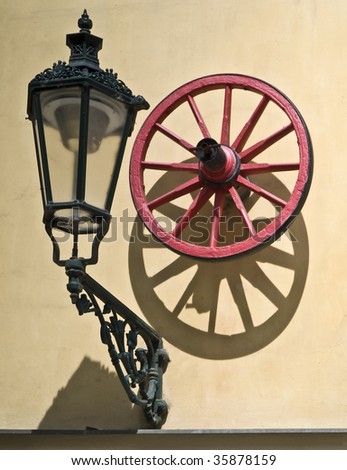 Facade of a rustic house with a lamp and a red wooden cart wheel