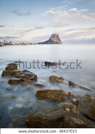 Vertical seascape showing the famous Rock of Ifach in the background, next to the buildings of the town of Calpe (Costa Blanca - Spain), including some rocks in the foreground.