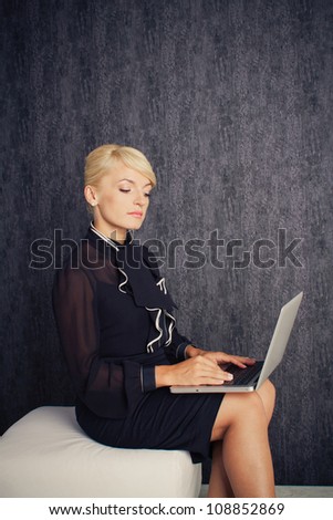 Blonde business woman sitting in black suit keep typing with laptop