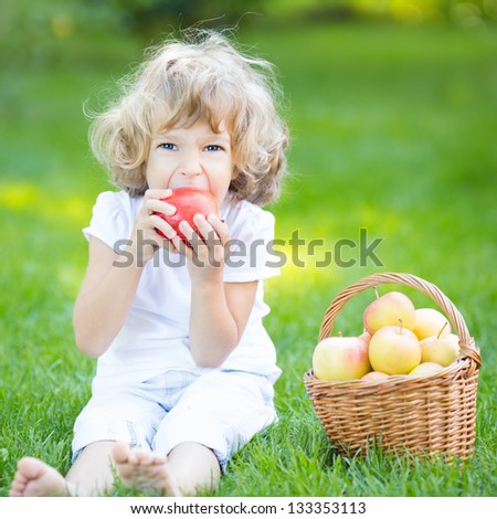 Happy child sitting on green grass and eating apple in spring park. Healthy lifestyle concept