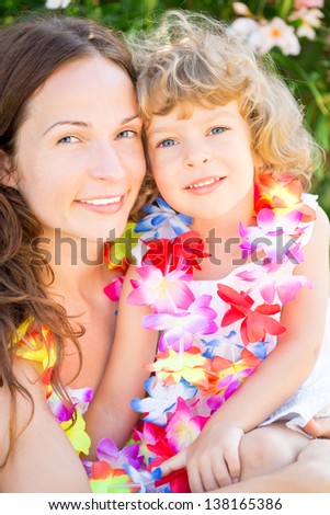 Happy child and mother wearing hawaiian flowers garland on the beach. Summer vacations concept