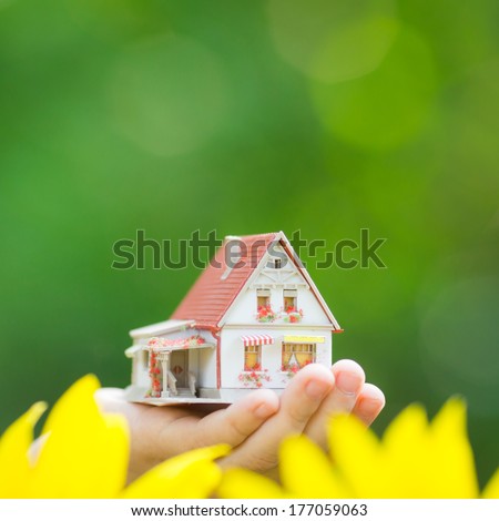 House in hand against spring green background. Real estate concept