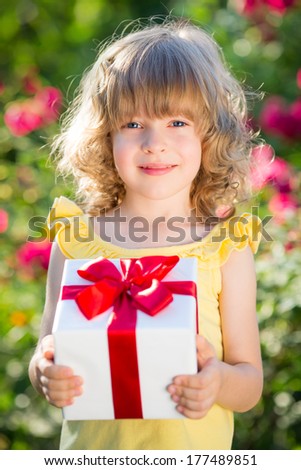 Child holding gift box against green background. Spring family holiday concept. Mother`s day
