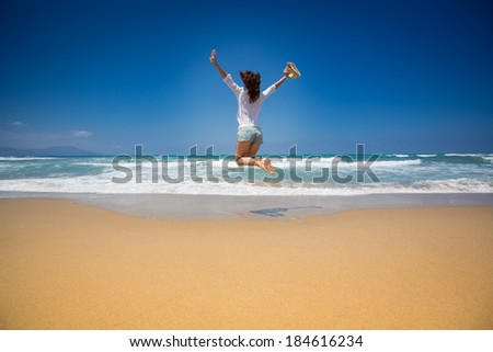 Happy woman jumping at the beach against blue sky and sea background. Summer vacations concept