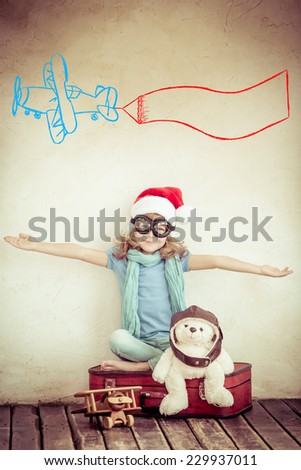 Happy child playing with toy airplane at home. Kid dressed in pilot against drawn plane on grunge wall background. Christmas holiday. Retro toned