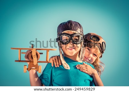 Happy kids playing with vintage wooden airplane outdoors. Portrait of children against summer sky background. Travel and freedom concept. Retro toned