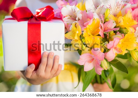 Gift box and flowers in hands against spring background. Family holiday concept. Mothers day