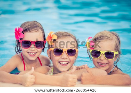 Happy children showing thumbs up in the swimming pool. Funny kids playing outdoors. Summer vacation concept