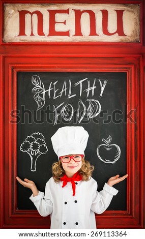 Child chef cook against blackboard blank menu with drawing healthy food. Restaurant business concept