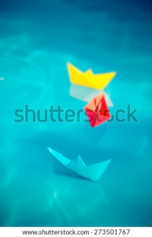 Multicolor paper sailing boats on blue water background. Summer vacation and travel concept. Toned image
