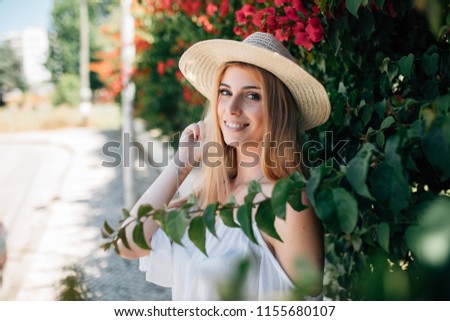 Young beautiful fashionable woman wearing straw hatl posing in street with flowering trees. Summer fashion concept. Stok fotoğraf © 