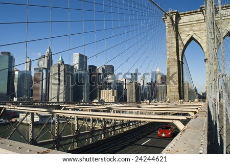 A red sports car crosses the Brooklyn Bridge with the Manhattan skyline in view.