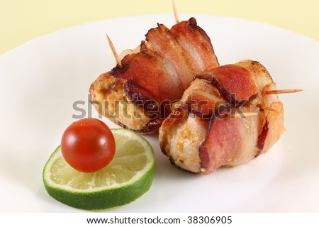 Arrangement of bacon wrapped chicken fillet with a slice of lime and cherry tomato