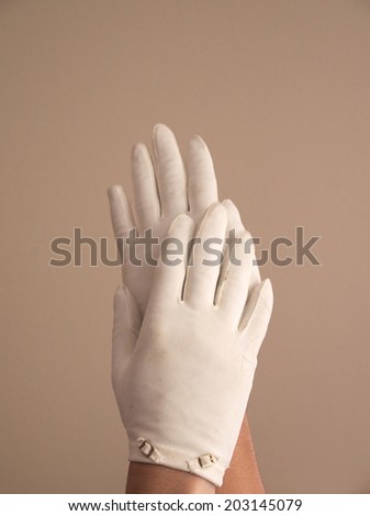 A woman\'s hands and forearms are shown as she models a vintage pair of formal white gloves with small buckles cuff. Her hands are overlapped.