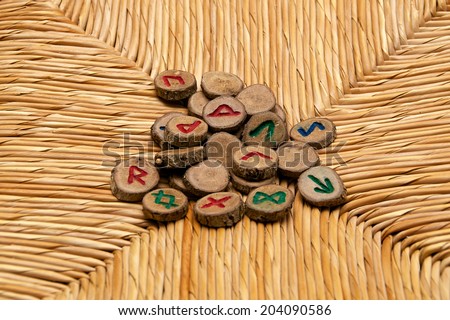 A pile of germanic runes, an ancient alphabet known as the futhark are on a woven rattan surface.